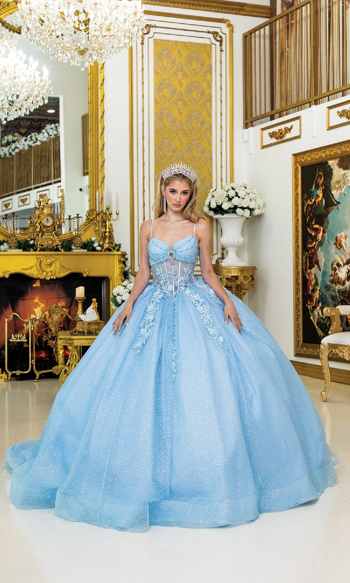 A woman in the Long Quinceañera Dress with Bow: Dancing Queen 1958 and a tiara stands in an ornate gold room adorned with chandeliers, a fireplace, and classical paintings.